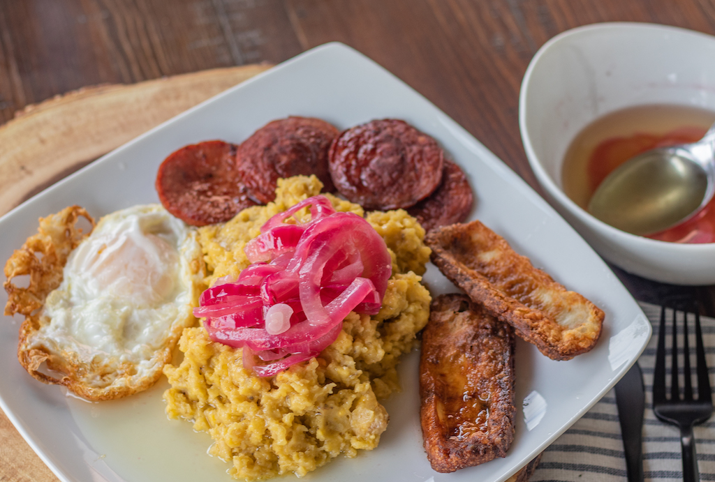 Plate with mashed plantains, fried egg, fried salami, fried cheese and topped with onion relish