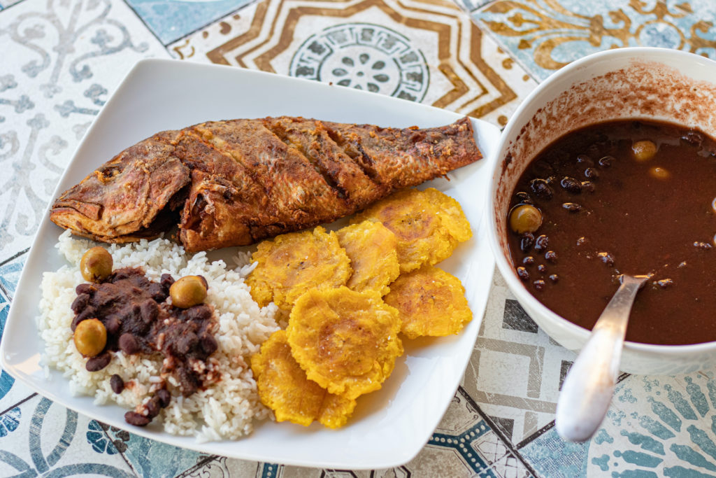 Fried red snapper with fried green plantains and rice and beans on a plate