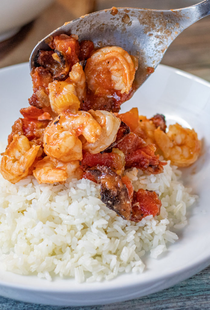 shrimp and bacon stew being served over white rice on a plate