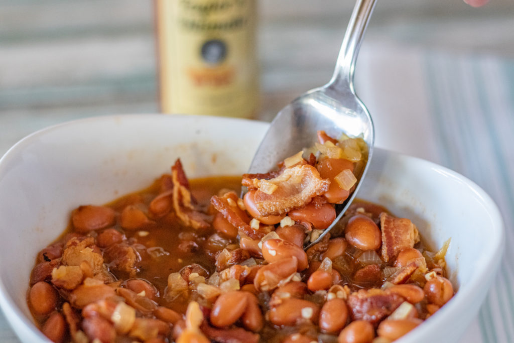 A bowl of beans with bacon. A spoonful is being taken from it.