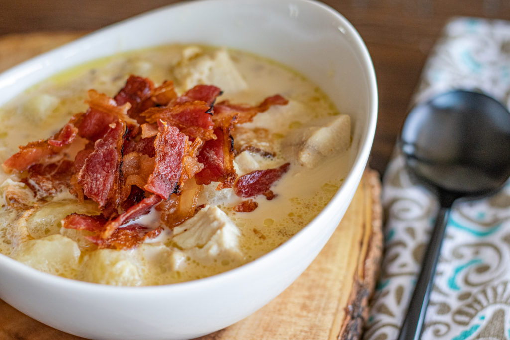 bowl of fish chowder with chopped bacon over top and a spoon on the right side