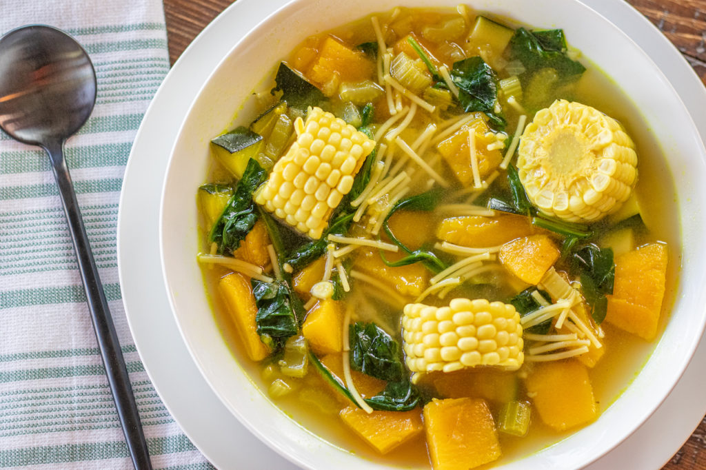 bowl of pumpkin soup made Latin style with pieces of corn on the cob and fideos.
