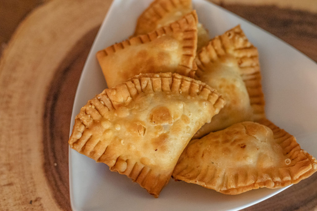 A plate with a few empanadas that are fried golden and filled with crab dip.