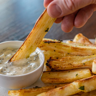 Close up of a hand dipping a baked yucca fry into mayo dipping sauce.
