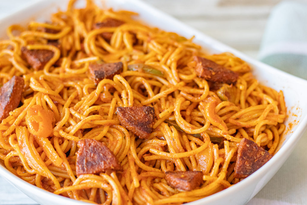 A large serving bowl filled to the brim and over the top with Dominican Spaghetti with salami.