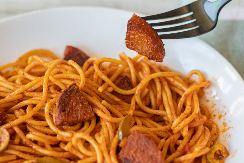 A plate of Dominican Spaghetti with Salami. A fork is sitting above it holding a piece of the Dominican Salami.