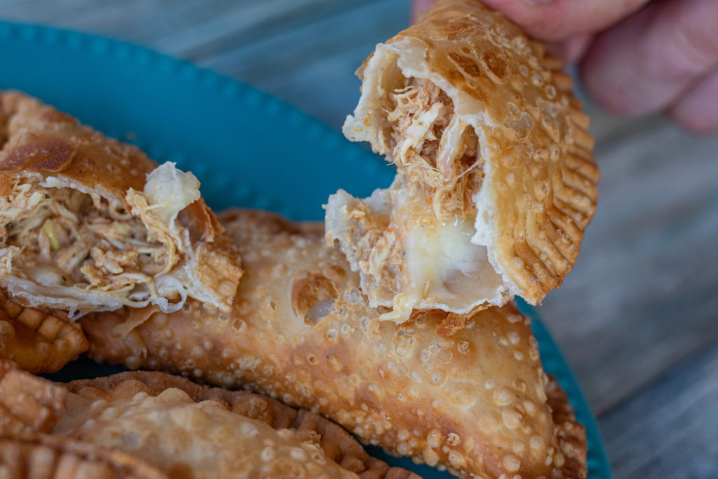 Dominican Chicken Empanadas with cheese with one of the empanadas cut in half. The image focuses into one of the halves. You can see the chicken, the cheese.