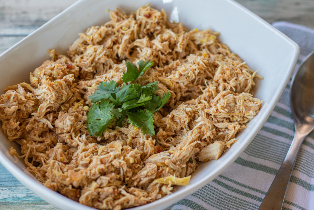 Latin Style Slow Cooker Chicken that's shredded after cooking, sitting in a large serving bowl with a little bit of cilantro sitting in the middle. This chicken is ready to join a rice and bean platter, a taco, an empanada... The possibilities are endless!