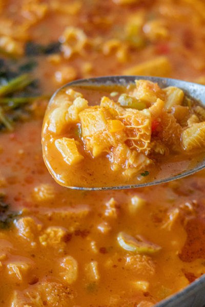 Dominican Mondongo (Stewed Tripe), in a large pot with a serving spoon being held close to the camera so you can see the texture of it.