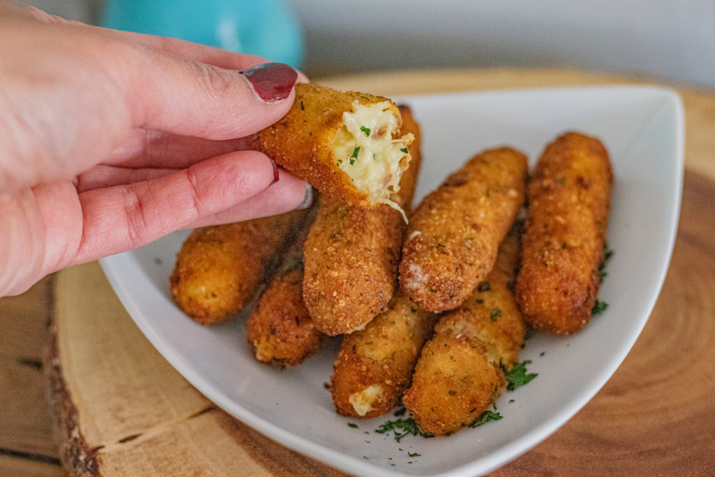 A platter of Latin Chicken Croquettes. One cut in half is being held up showing its inside.