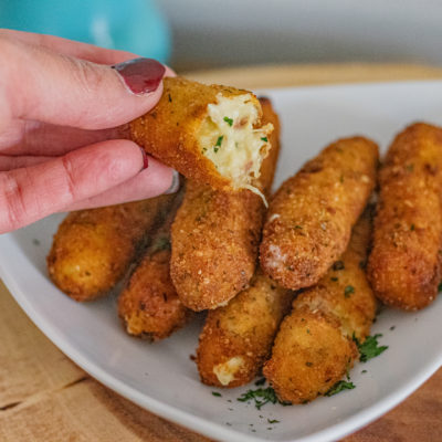 A platter of Latin Chicken Croquettes. One cut in half is being held up showing its inside.