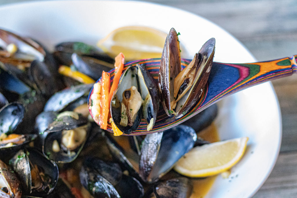 Loaded Mussels with shallots, garlic, peppers, corn, wine, chicken broth and more! This image is a close up of the finished dish with the mussels now open and ready to serve.