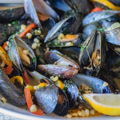 Loaded Mussels with shallots, garlic, peppers, corn, wine, chicken broth and more! This image is a close up of the finished dish with the mussels now open and ready to serve.