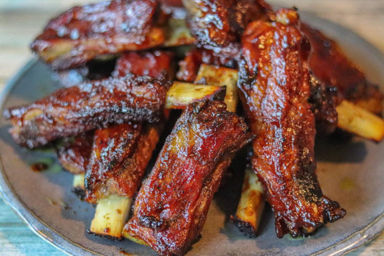 Dominican Barbecue Ribs cut in single pieces. In the picture they are layered one over the other and you can see the bones and the meat glistening from the barbecue sauce.