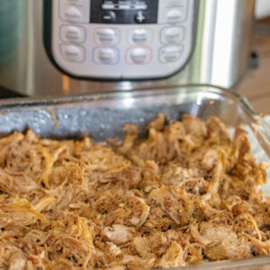 Instant Pot Dominican Pernil (Pulled Pork). Its shredded in a baking dish. You can see the instant pot in the background.