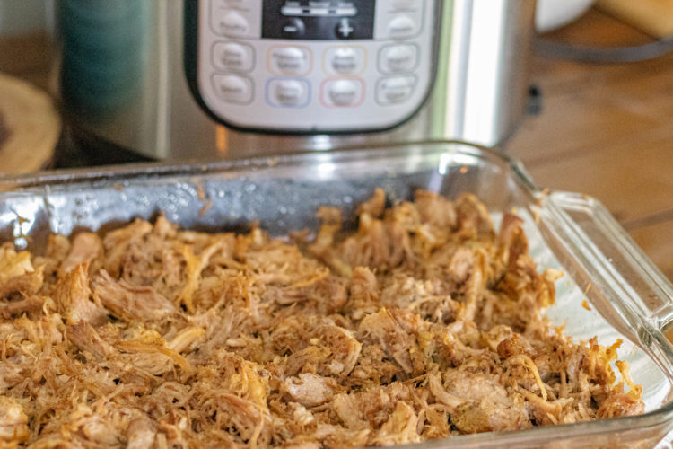 Instant Pot Dominican Pernil (Pulled Pork). Its shredded in a baking dish. You can see the instant pot in the background.
