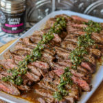 Skirt Steak with Chimichurri. Here you see the skirt steak sliced and laid out in two rows with chimichurri sauce in the center of each row. You can also see the Casa m Spice container next to the platter.