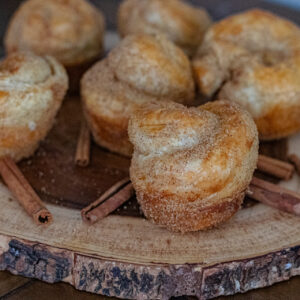 Easy Churro Popovers on a wooden serving board. You can also see some whole cinnamon sticks sitting all around them.