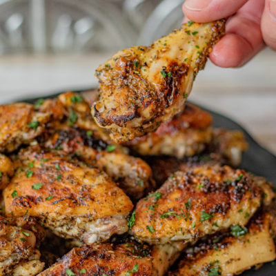 Italian Glazed Chicken Wings on a plate and a hand is holding a drumstick over the plate.