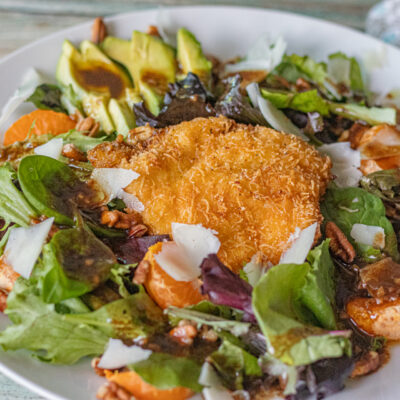 A single serving of Crispy Chicken Salad. Ingredients include a crispy italian seasoned thin chicken slice, mandarine oranges, avocado slices, shaved manchego cheese, pecans chopped basil, mixed greens with a homemade balsamic vinaigrette dressing. Absolutely delicious!