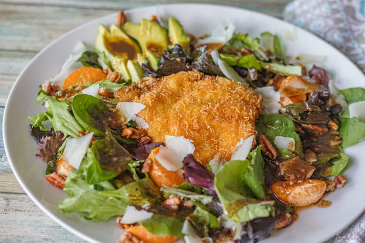 A single serving of Crispy Chicken Salad. Ingredients include a crispy italian seasoned thin chicken slice, mandarine oranges, avocado slices, shaved manchego cheese, pecans chopped basil, mixed greens with a homemade balsamic vinaigrette dressing. Absolutely delicious!