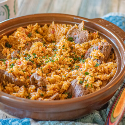 One Pan Latin Beef and Rice in a serving dish. You can see the beautiful orange rice with thin slices of steak all around and topped with very finely chopped cilantro.