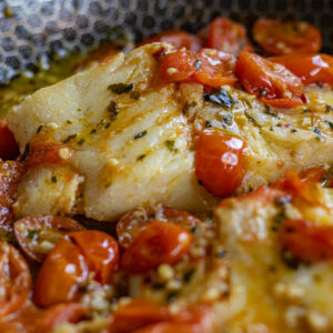 Tomato Basil Cod in the skillet it was cooked in. Very close up shot to capture the details of the flaky cod in the tomato basil sauce.