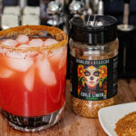 Chile Limon Watermelon Paloma next to the Chile Limon seasoning used to rim the glass. That is Spanglish Asadero Chile Limon. You can find on Amazon.