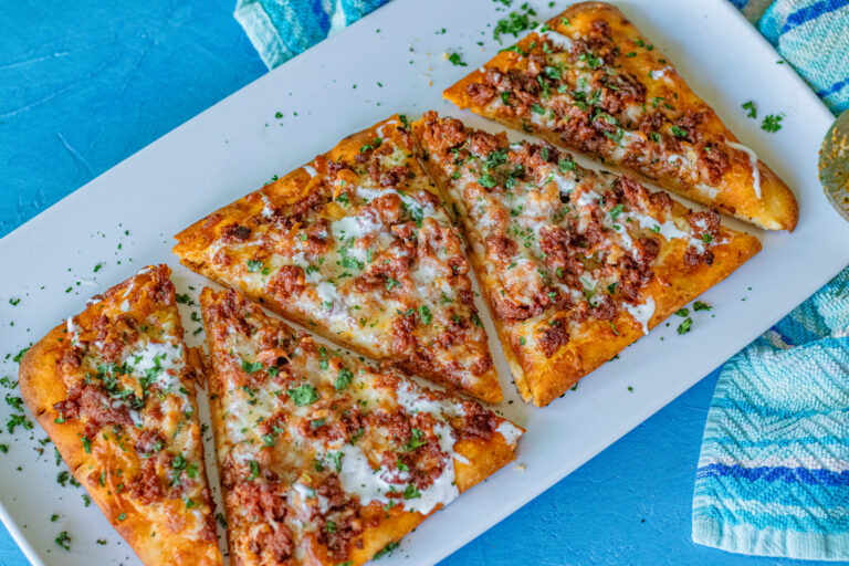 Chorizo flatbread sitting on a serving plate and cut into 5 triangles. The flatbread was brushed with olive oil and garlic, then topped with shredded mozzarella, cooked ground chorizo, Mexican Cheese blend, Mexican crema and sprinkled with finely chopped cilantro. An absolute family favorite in our home.