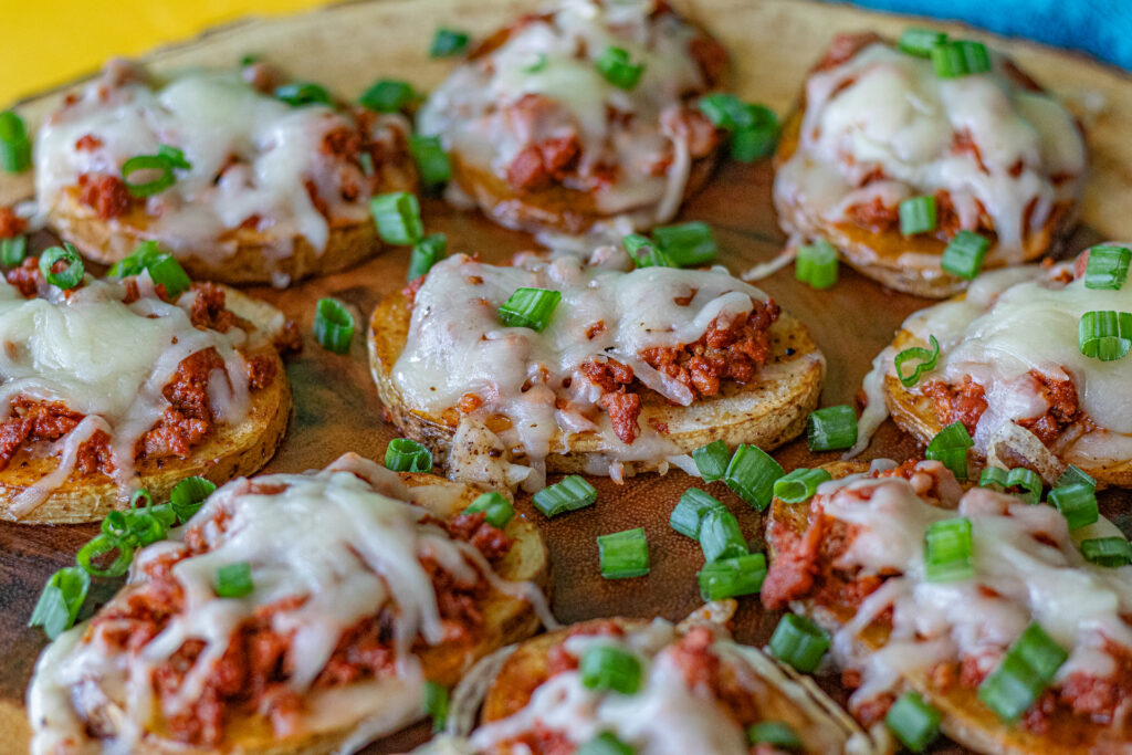 Chorizo Baked Potato Slices on a serving platter. You can see the potato slices are topped with chorizo, melted cheese and chopped green onions. Looks delicious!