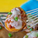 A Chorizo Baked Potato Slice being held up. You can see the potato slice is topped with chorizo, melted cheese and chopped green onions. Looks delicious!