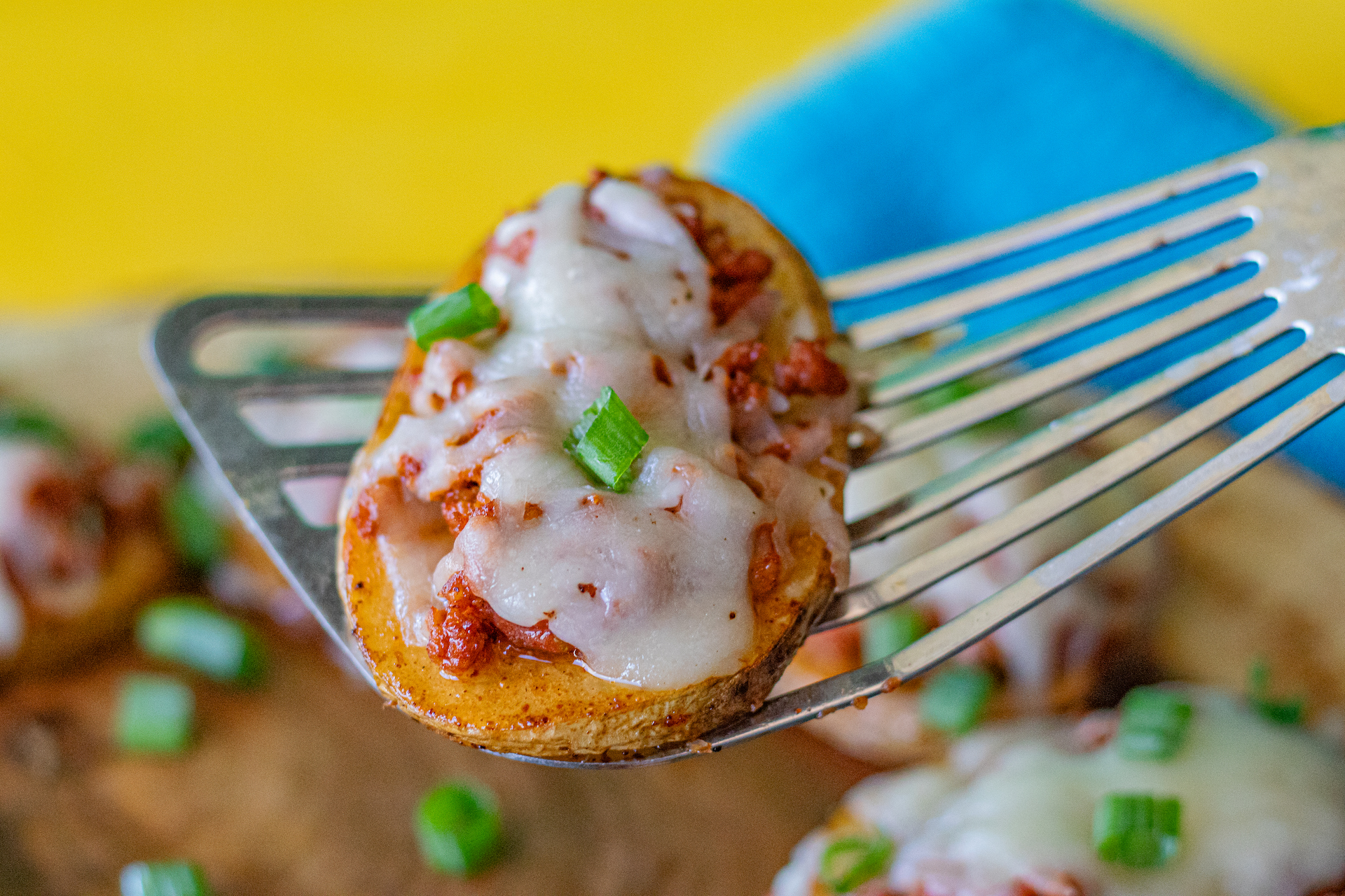 A Chorizo Baked Potato Slice being held up. You can see the potato slice is topped with chorizo, melted cheese and chopped green onions. Looks delicious!