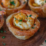 Stewed Shrimp Yuca Cup on a wooden tray. You can see the shrimp, tail on in the cup and topped with some chopped cilantro.