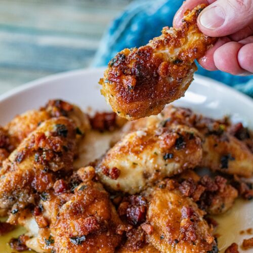 Chicken Marsala Wings with Pancetta. A hand is holding a drumstick up. You can see the bits of pancetta over the wings as well. Delicious!