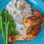 Rosemary Lemon Chicken leg quarter with green beans and mashed potatoes on a bright blue plate. Looks delicious!