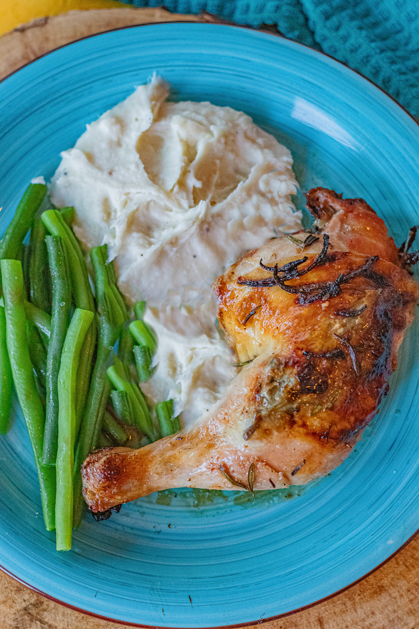 Rosemary Lemon Chicken leg quarter with green beans and mashed potatoes on a bright blue plate. Looks delicious!