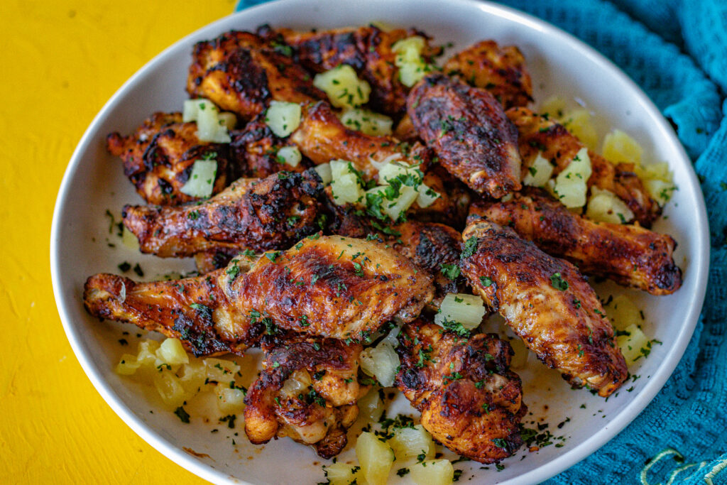 Al Pastor Chicken Wings on a serving plate. You can see the chopped up pineapple and chopped cilantro as garnishes.