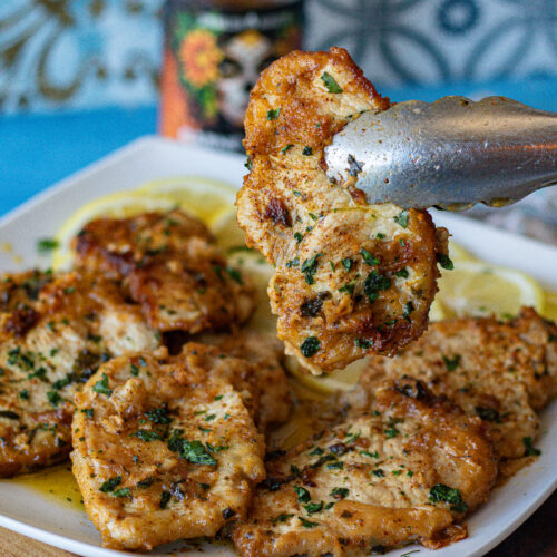 Lemon Carne Asada Pork Chops on a plate over lemon wedges. 8 pieces that are thin and boneless. One is being held up to show its deliciousness.