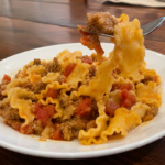 drunken italian sausage and noodles in a serving plate. Made with Malfadine pasta. And you can see the pasta and some sausage being held up by a fork.